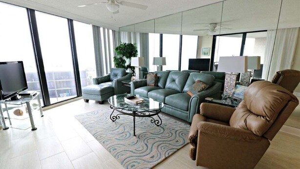 A modern living room with a sofa, armchairs, a coffee table, and a TV. - Miles of Wide Sandy Beaches! Anastasia Condos 603 (St Augustine)