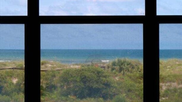 A view through a window with a grid pattern, overlooking a beach and ocean. - Oceanfront Charm in Barefoot Trace 114 (St. Augustine)