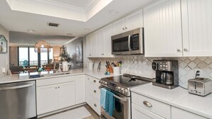 Una cucina moderna con mobili bianchi, piano cottura in acciaio inossidabile, forno a microonde e macchina da caffè.