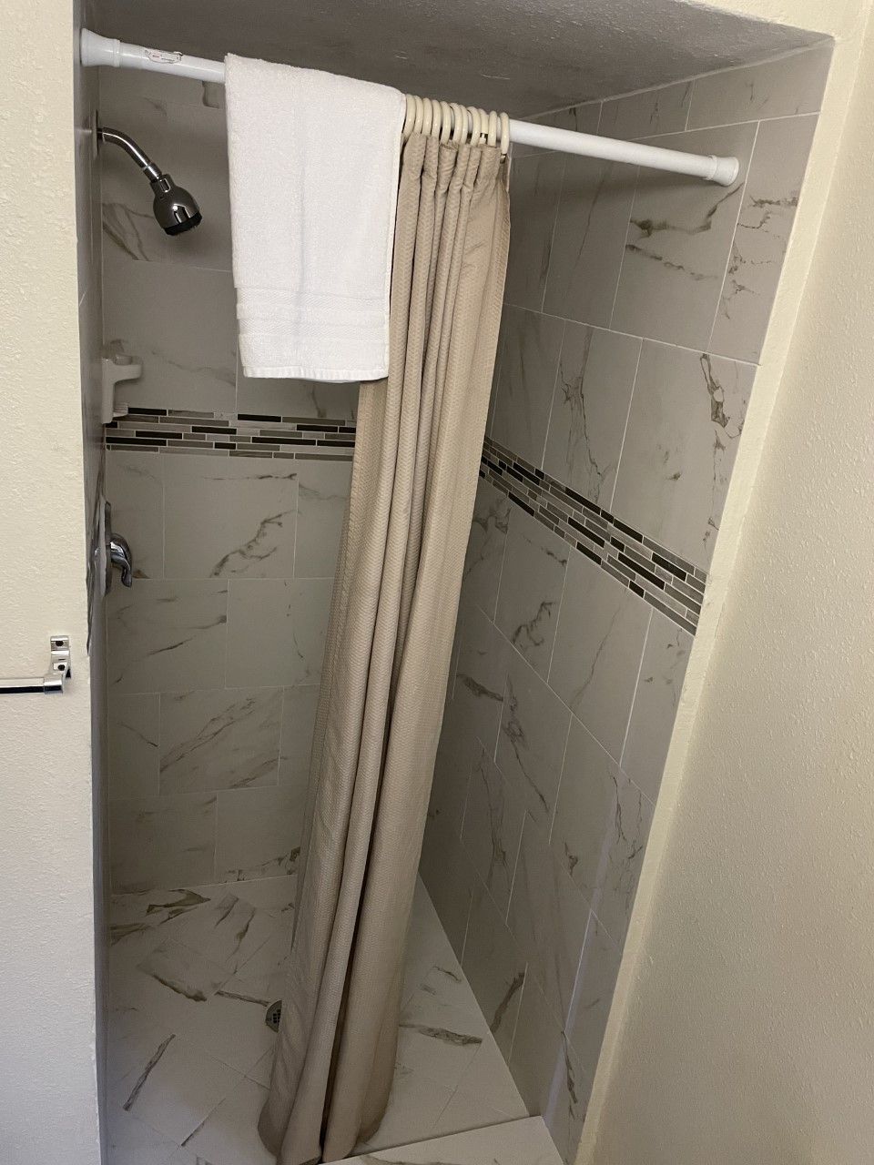 Un área de ducha con cortina color crema, un cabezal de ducha de mano y paredes con azulejos.
