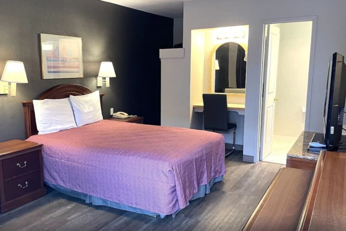 A hotel room with a bed, bedside tables, a desk with a chair, a television, and a mirror.