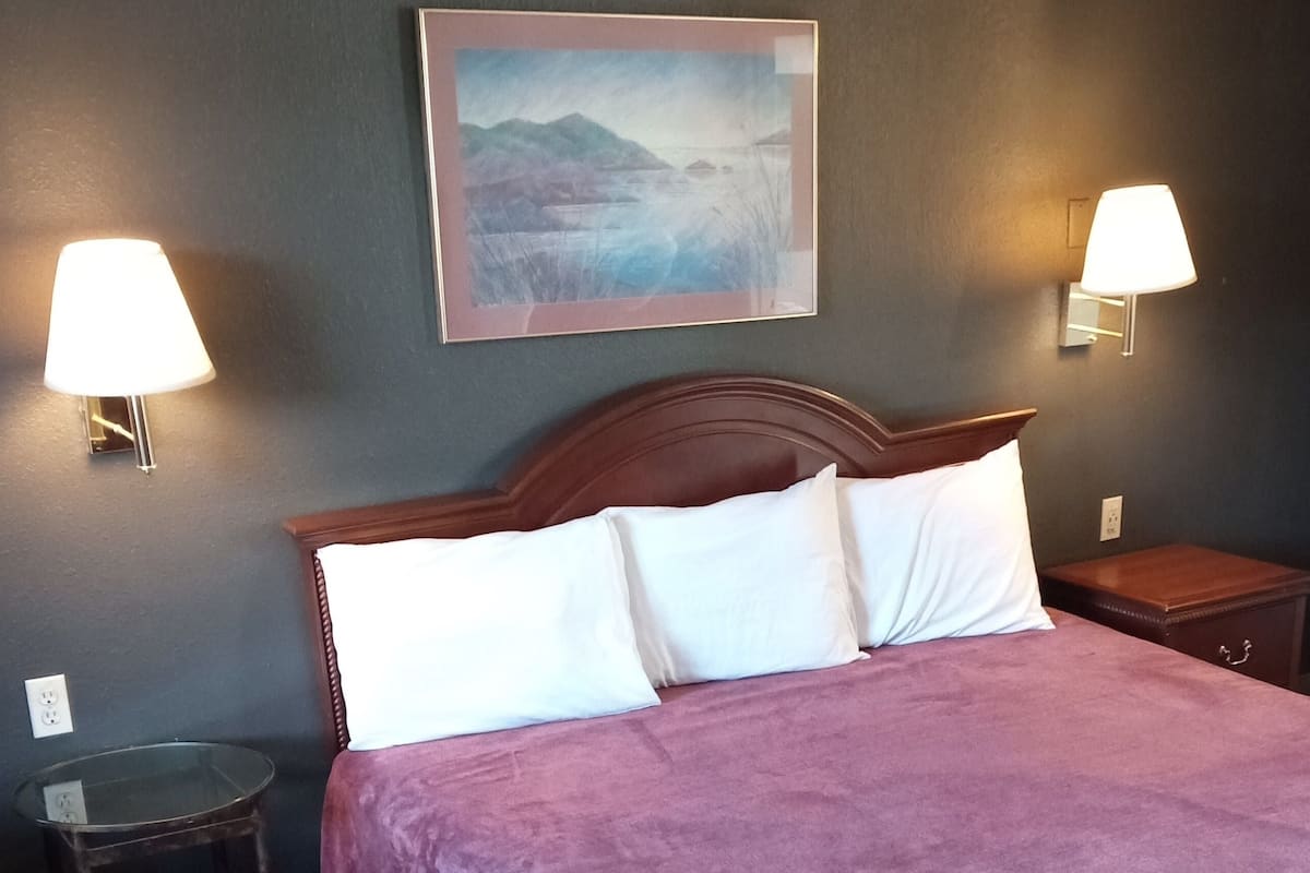 A hotel room with a bed, two bedside lamps, a nightstand, and a framed picture on the wall.