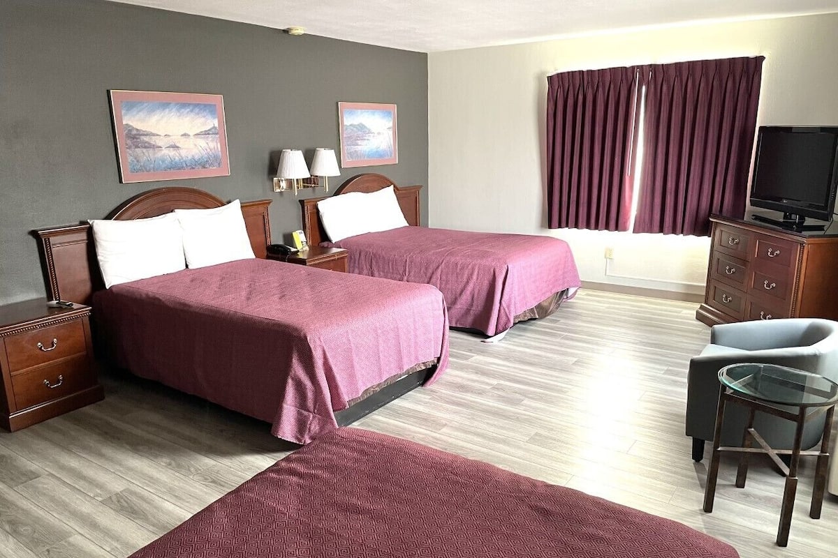 A hotel room with two beds, a desk, a chair, a TV, and artwork on the walls.