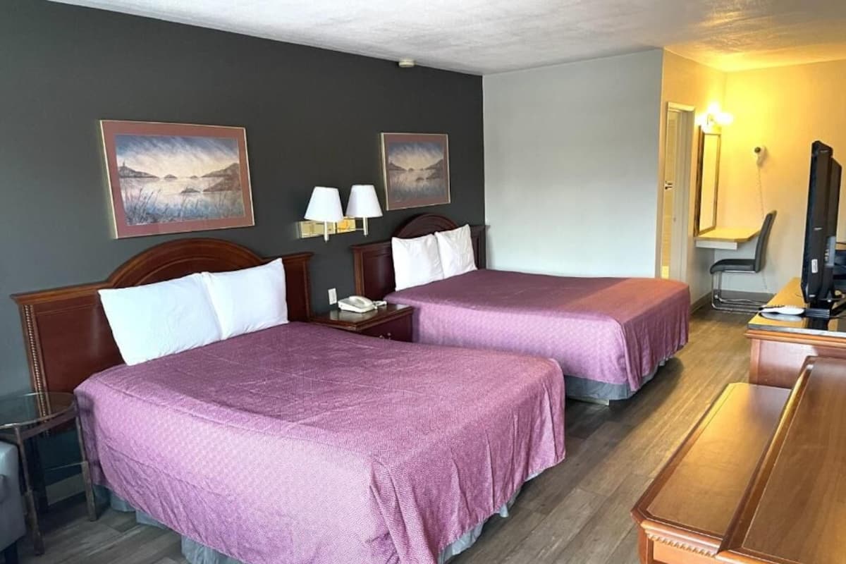A hotel room with two beds, a desk, a chair, a TV, and two paintings on the wall.