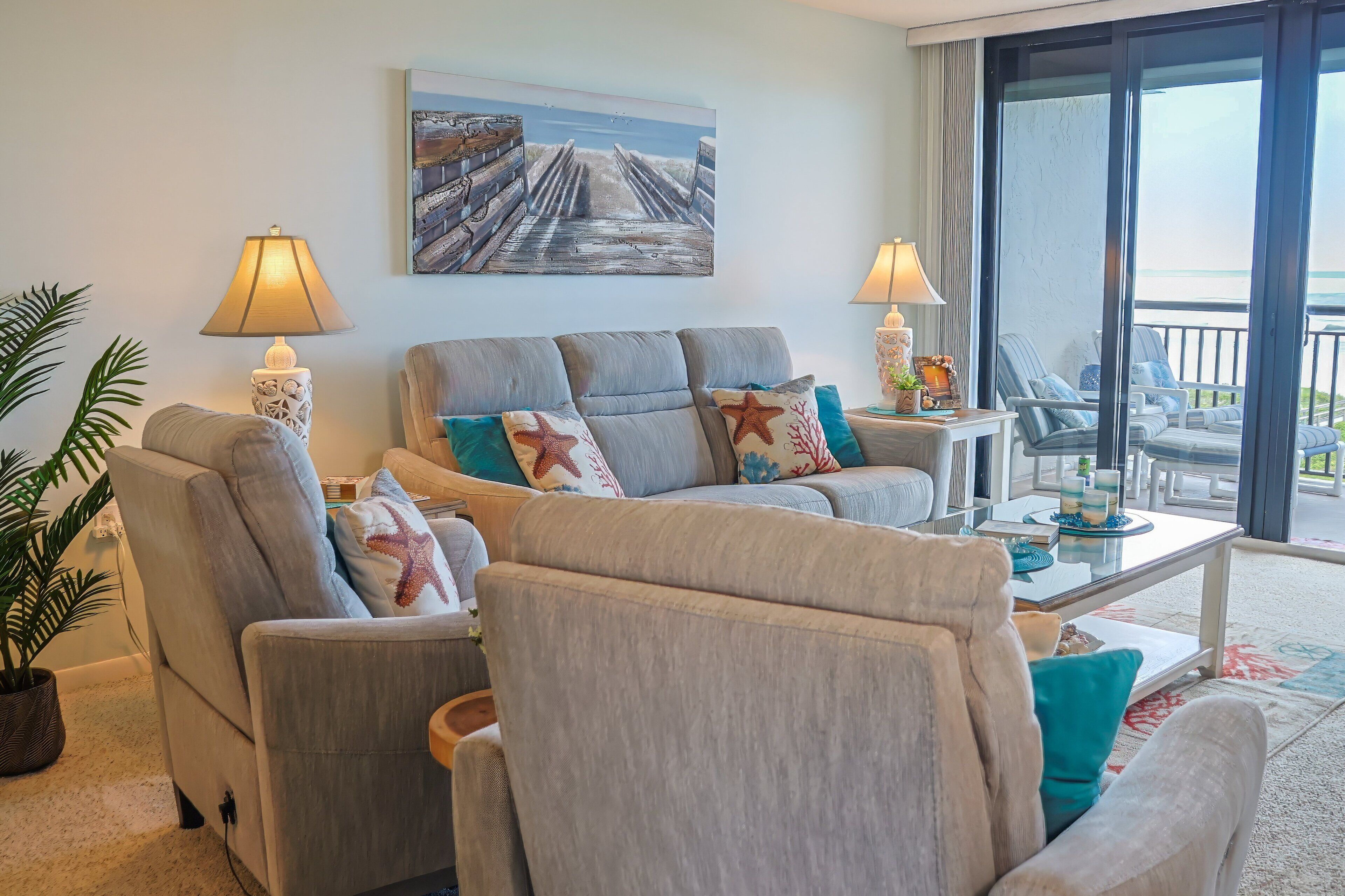 A living room with a sofa, armchairs, a coffee table, lamps, a painting, and a view of the outdoors.
