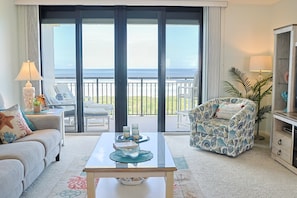 A room with a sofa, armchair, and a table with decorative items. There is a large window with a view of the ocean. - Barefoot Trace 410-Luxury, Direct Oceanfront Two Bedroom Condo (St. Augustine)