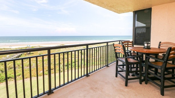 Ein Balkon mit Blick auf den Strand, einem Tisch mit Stühlen und einem Fenster.