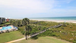 Blick auf einen Strand mit Pool, Palmen und einer Holzpromenade.