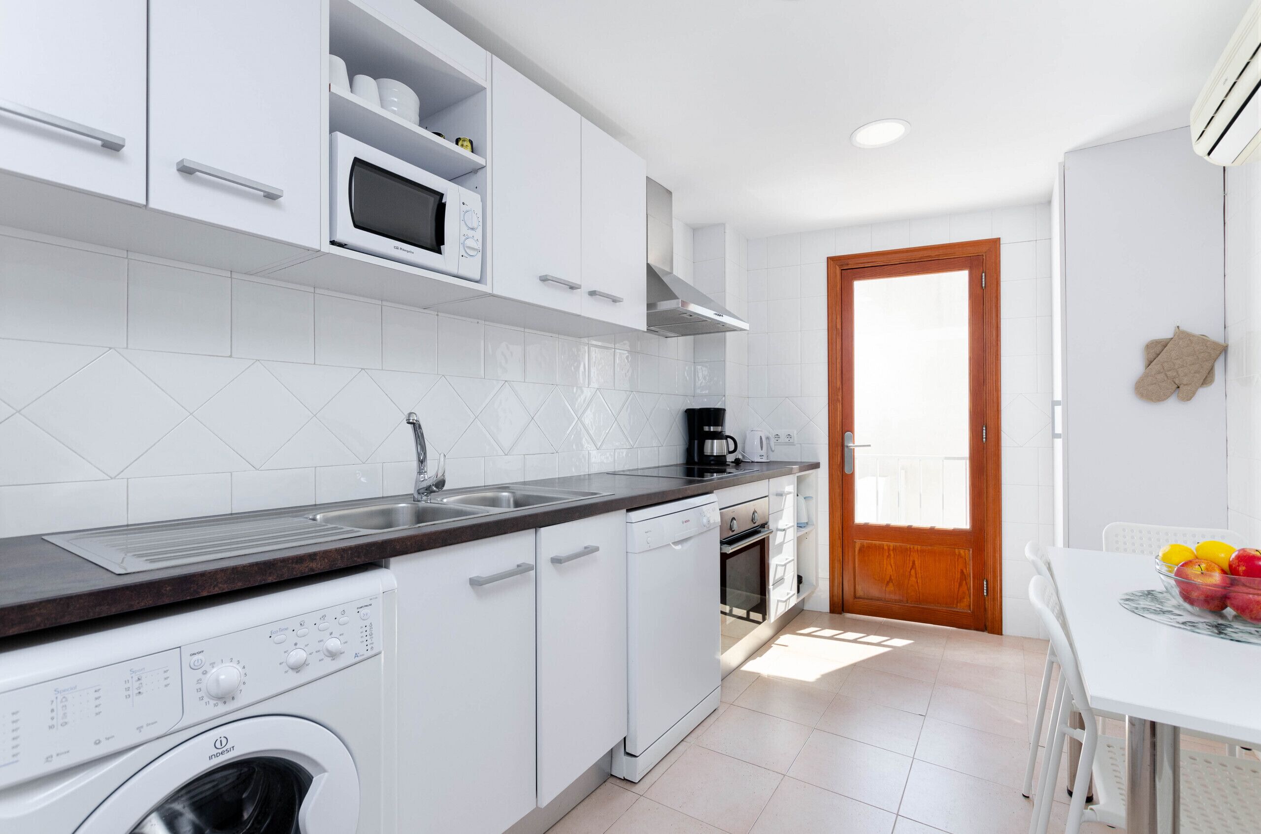 Une cuisine compacte avec des meubles blancs, un four à micro-ondes encastré, une machine à café et un lave-linge.