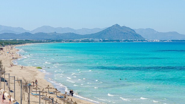 A beach with clear turquoise waters, a sandy shore, and mountains in the background. - YourHouse Blaublue 2.3, wonderful sea view apartment in Majorca North (Can Picafort)