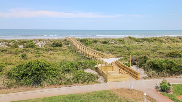 Een houten looppad leidt naar een strand met duinen en een helder uitzicht op de oceaan.