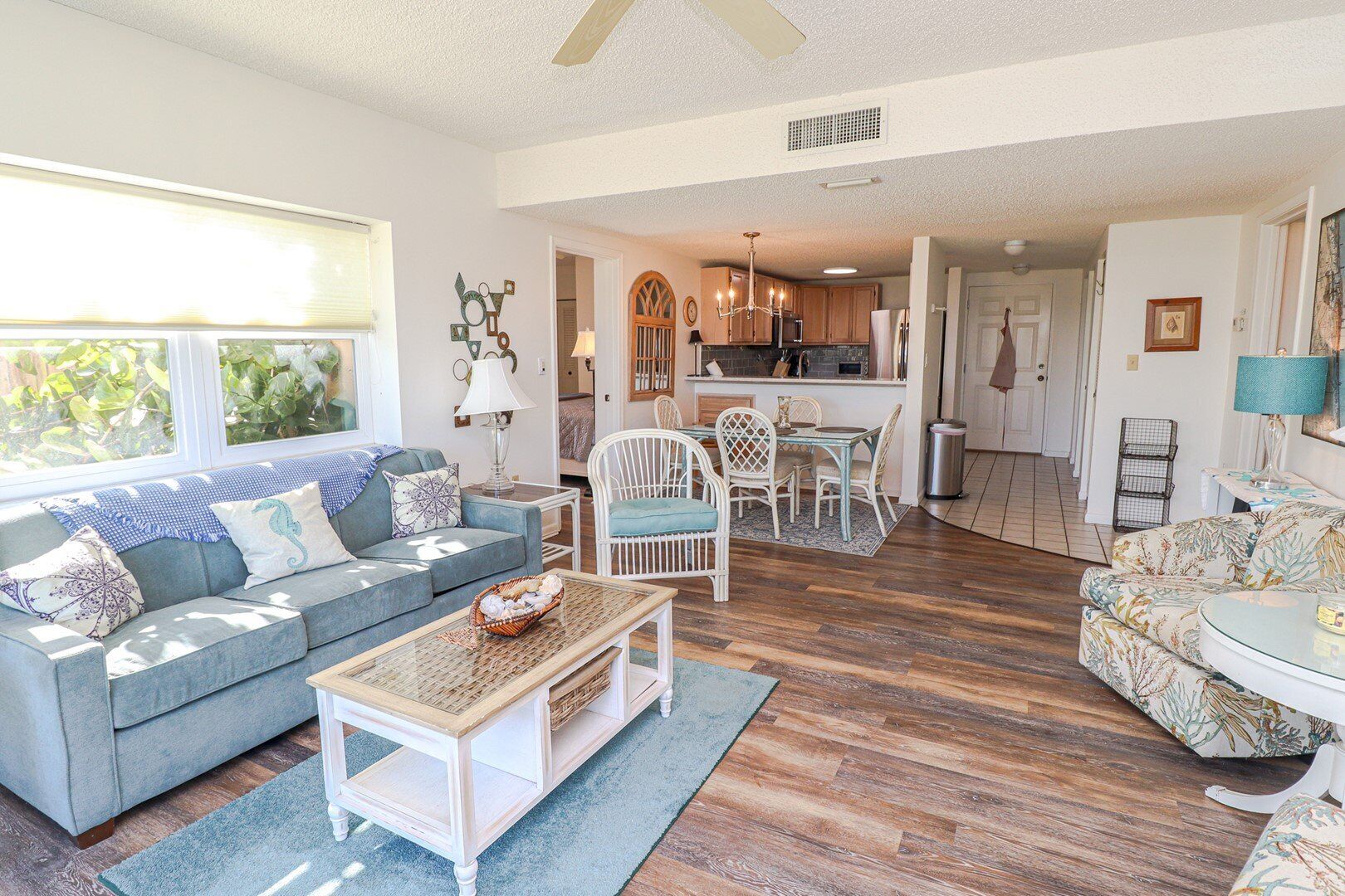 A spacious living room with a blue sofa, white chairs, and a dining area with a table and chairs.