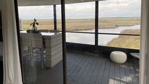 Una habitación con un amplio ventanal que da a una terraza con vistas a un paisaje pantanoso.