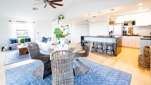 Una cocina moderna con una isla central, taburetes de bar y un área de comedor con sillas de mimbre.