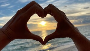 Manos formando un corazón sobre el atardecer en la playa.