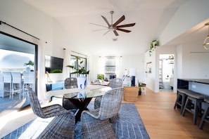 Relax in a spacious living area with a glass dining table and comfortable seating, featuring a large flat-screen TV and fireplace.
