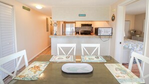 Cocina compacta con refrigerador, estufa y microondas. Hay una mesa de comedor con sillas y posavasos.