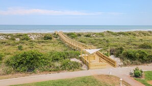 Une promenade en bois qui mène à une plage, avec un système de dunes et une vue dégagée sur l’océan.