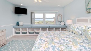 Une chambre avec un lit, une fenêtre donnant sur un beau paysage, un ventilateur de plafond et un téléviseur fixé au mur.