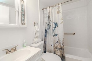 Une salle de bain avec un lavabo blanc, des toilettes, une baignoire et un rideau de douche orné de motifs marins.