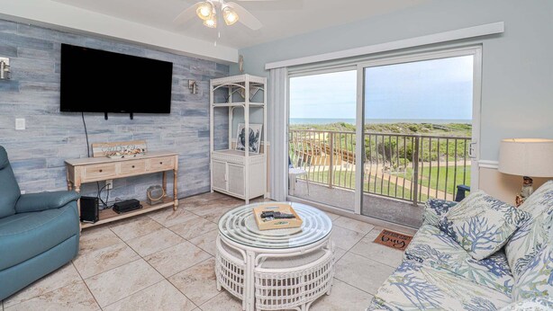 Un salon équipé d’un téléviseur à écran plat, d’un ventilateur de plafond, d’un canapé, d’une table basse et d’un balcon avec vue.