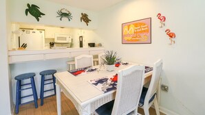 Cocina compacta con armarios blancos, microondas y un pequeño comedor con una mesa y dos taburetes.