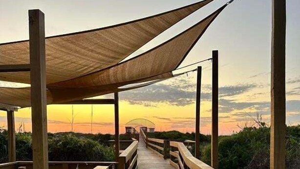 Un paseo marítimo de madera que conduce a una zona cubierta con vista al atardecer.