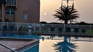 A swimming pool with a clear reflection, a palm tree, and a building in the background. - Enjoy this one bedroom condo overlooking the pool, Creston House 5A (St. Augustine)