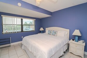 Une chambre avec un grand lit, deux tables de chevet, une fenêtre avec des stores et un radiateur.