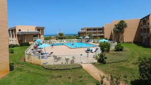 Un resort con una piscina centrale circondata da lettini e ombrelloni, affacciato sull'oceano.