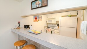 Una cucina con piano di lavoro in marmo, fornello, forno a microonde e frigorifero. Ci sono due sgabelli di legno e un tavolino.