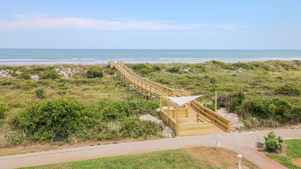 Ein Holzsteg führt zu einem Strand mit Dünen und freiem Blick auf den Ozean.