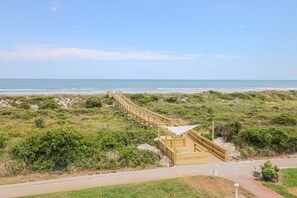 Un muelle de madera que conduce a una playa con dunas y una vista despejada del océano.