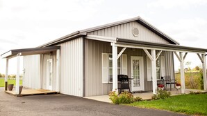 A single-story building with a covered porch, a door, and a small outdoor seating area with a grill.