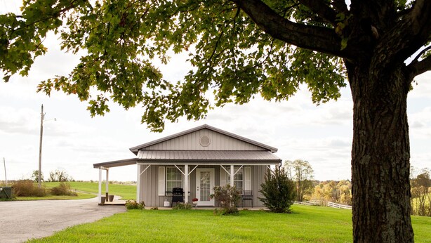 A single-story house with a porch, a lawn, and a tree in the foreground.