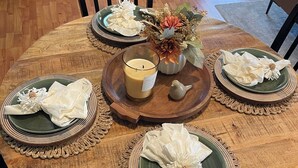 A round dining table with green plates, white napkins, and a candle centerpiece.