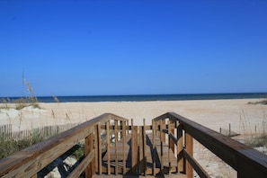 A wooden boardwalk leading to a sandy beach with clear blue skies.