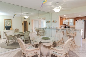 A dining area with wicker chairs and a glass table, a kitchen with a microwave and refrigerator, and a ceiling fan.