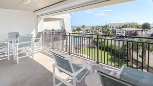 A balcony with white wicker furniture, a pool, and a view of a residential area with palm trees. - Island South 33 Ocean View Condo On Third Floor (St. Augustine)