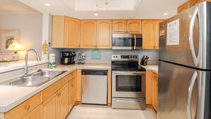 A modern kitchen with wooden cabinets, stainless steel appliances, a dishwasher, a coffee maker, and a sign that reads "Beach House." - Island South 33 Ocean View Condo On Third Floor (St. Augustine)