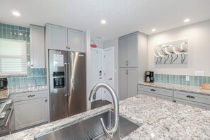 A modern kitchen with stainless steel appliances, granite countertops, and a view of the beach through the window.