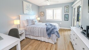 Une chambre à coucher comprenant un lit, des tables de chevet, un bureau, une commode et un ventilateur de plafond.