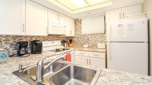 Una cucina moderna con mobili bianchi, lavello in acciaio inossidabile, forno integrato, frigorifero e un lucernario.