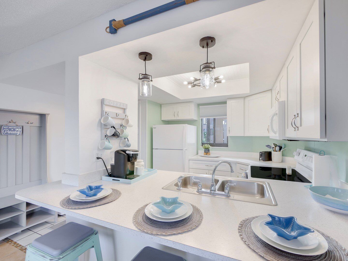 A modern kitchen with white cabinets, a central island with a sink, and a coffee station.