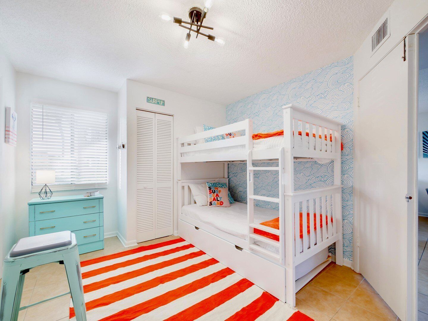 Un dormitorio infantil con literas, un escritorio y una alfombra a rayas.