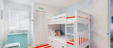 Un dormitorio infantil con literas, un escritorio y una alfombra a rayas.