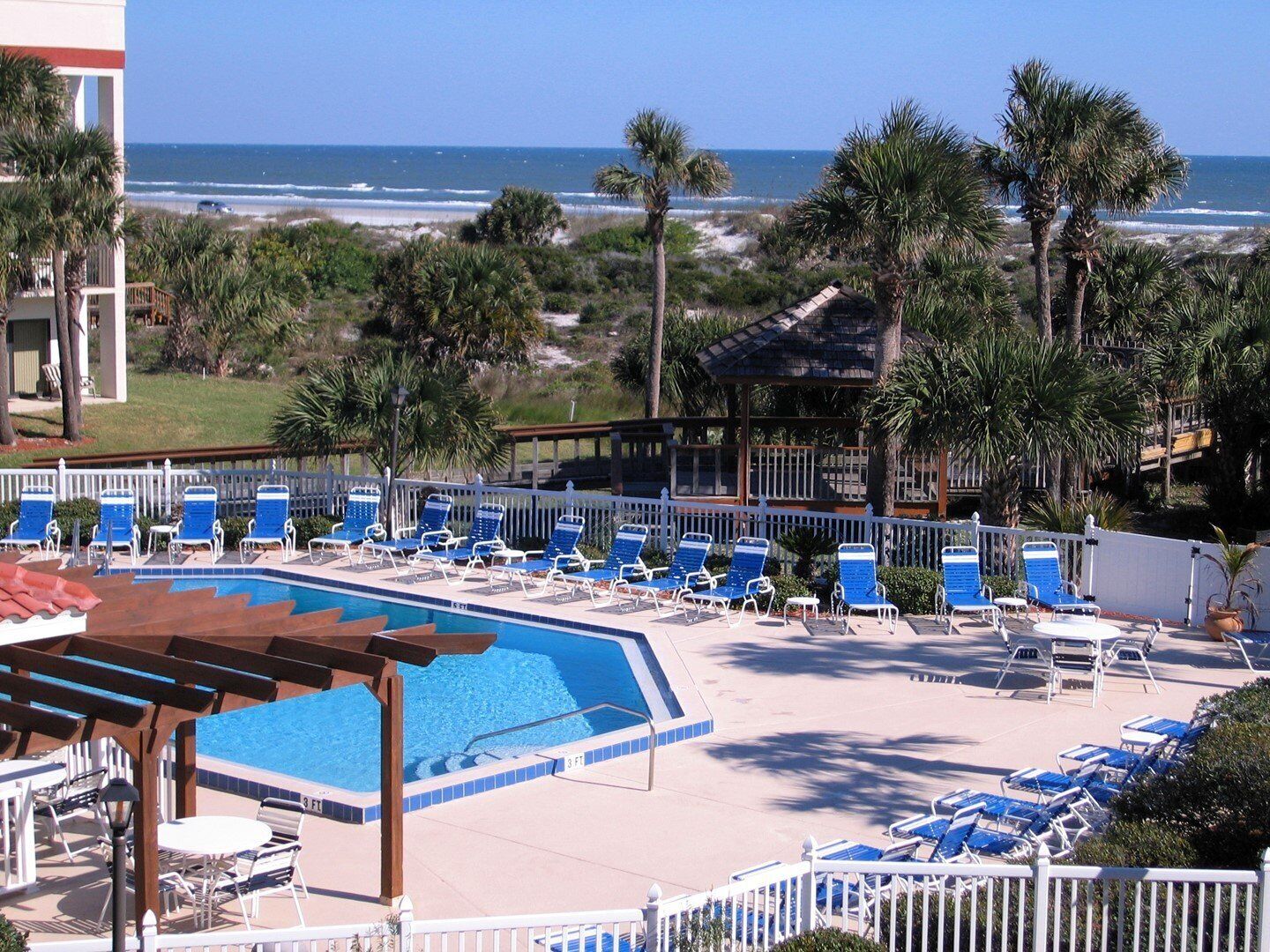 A pool area with blue lounge chairs and a view of the ocean.