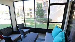 A sunlit patio with wicker furniture, large windows, and a view of a residential area. - Ocean Village Club Condo D17 (St. Augustine)