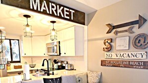 A dining area with a wooden table and blue stools, a kitchen in the background, and a wall sign indicating 'NO VACANCY' at St. Augustine Beach. - Ocean Village Club Condo D17 (St. Augustine)