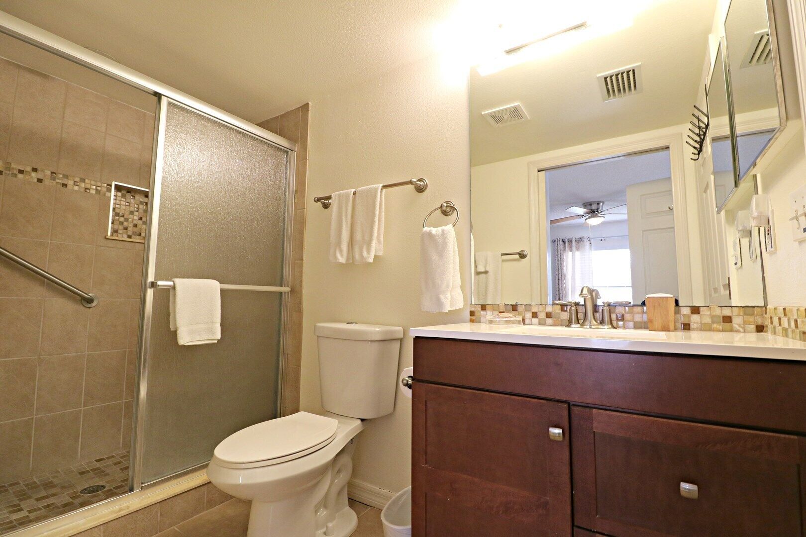 A bathroom with a glass shower enclosure, a toilet, a vanity with a mirror, and a towel rack.